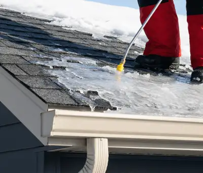 Ice dam removal technician using a steam wand to melt thick ice buildup on a residential roof in Indianapolis, IN