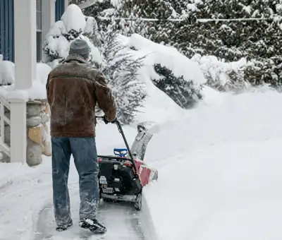 Residential snow removal technician using a snow blower to clear a home driveway and walkway in Indianapolis, IN