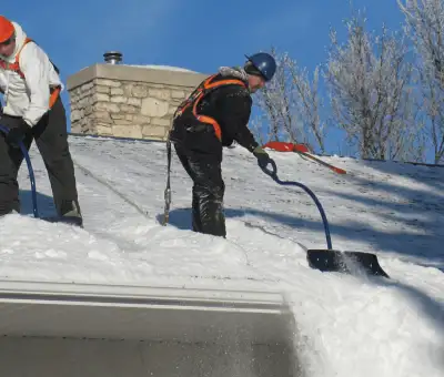 Professional technicians performing roof snow removal with safety harnesses and shovels in Indianapolis, IN